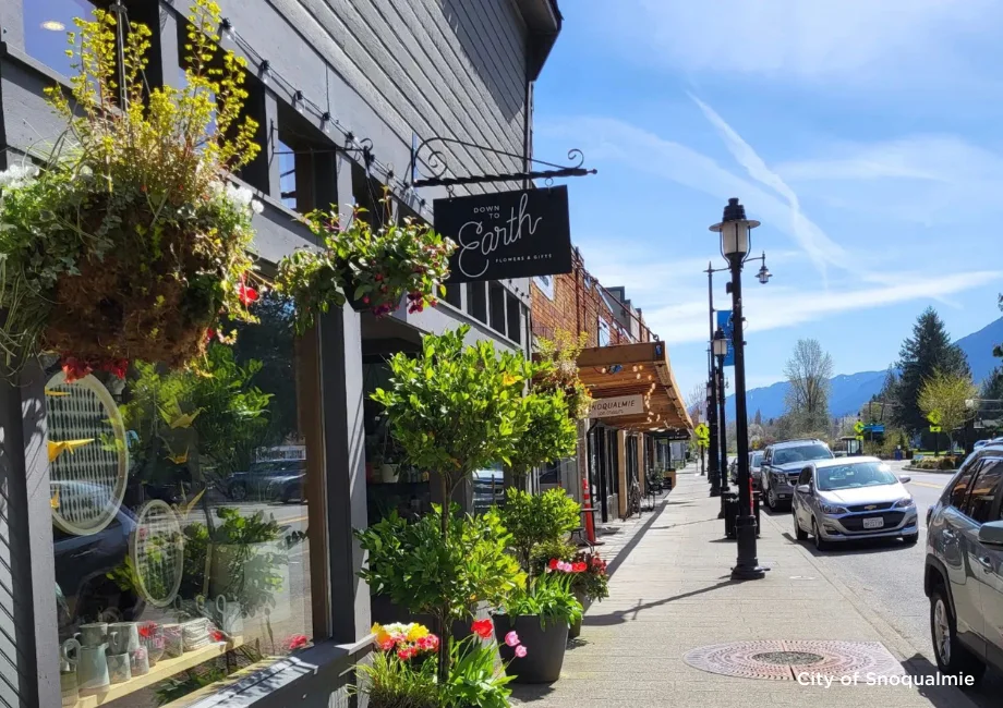 Flower baskets and storefronts along a sunny sidewalk in historic Downtown Snoqualmie