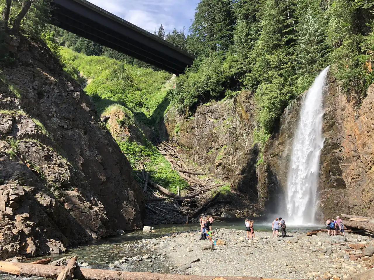 Franklin Falls dropping down a rock wall into a shallow pool, with hikers on the gravel bar
