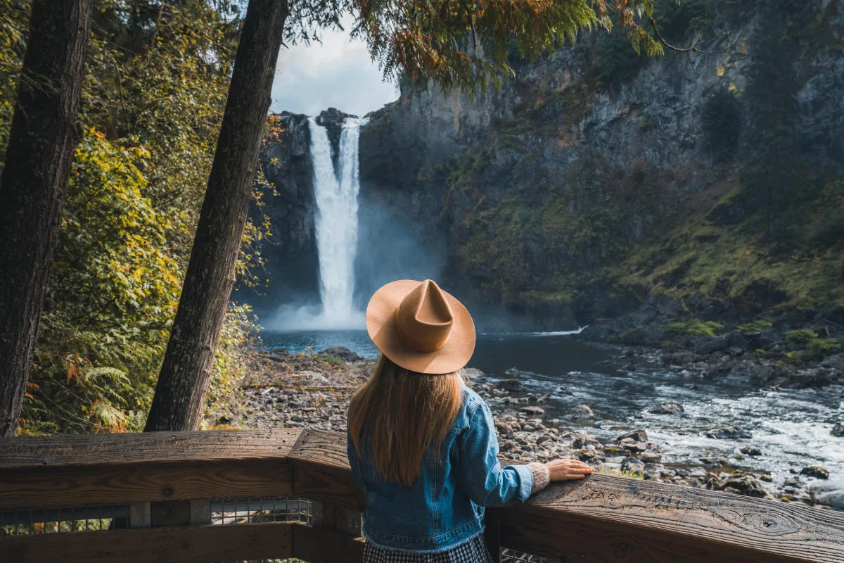 Visitor in a tan hat looking toward Snoqualmie Falls from the lower viewing platform