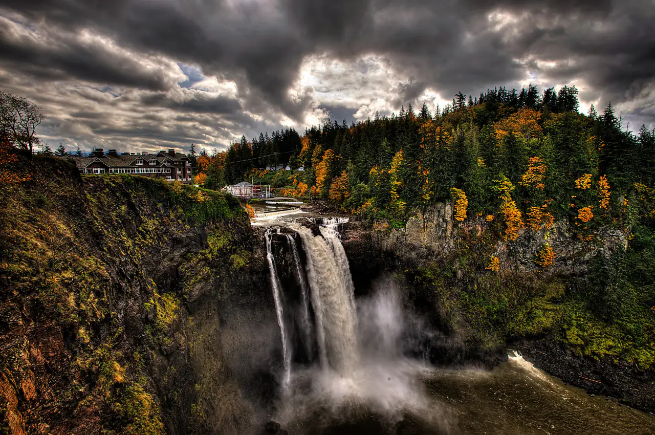 Snoqualmie Falls and the lodge under dramatic storm clouds, with autumn colors on the cliffs