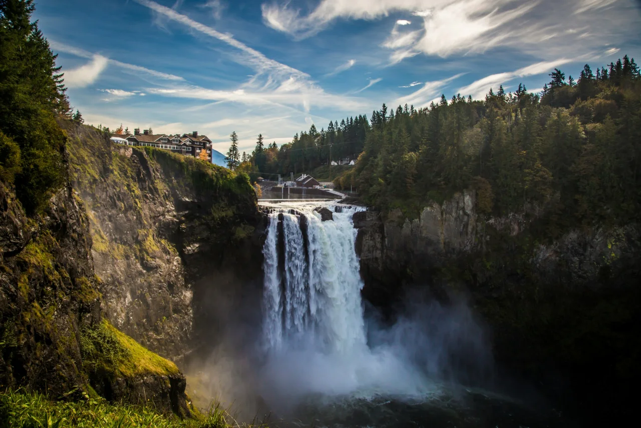 Snoqualmie Falls dropping into a mist-filled gorge beneath Salish Lodge, forested cliffs and a blue sky