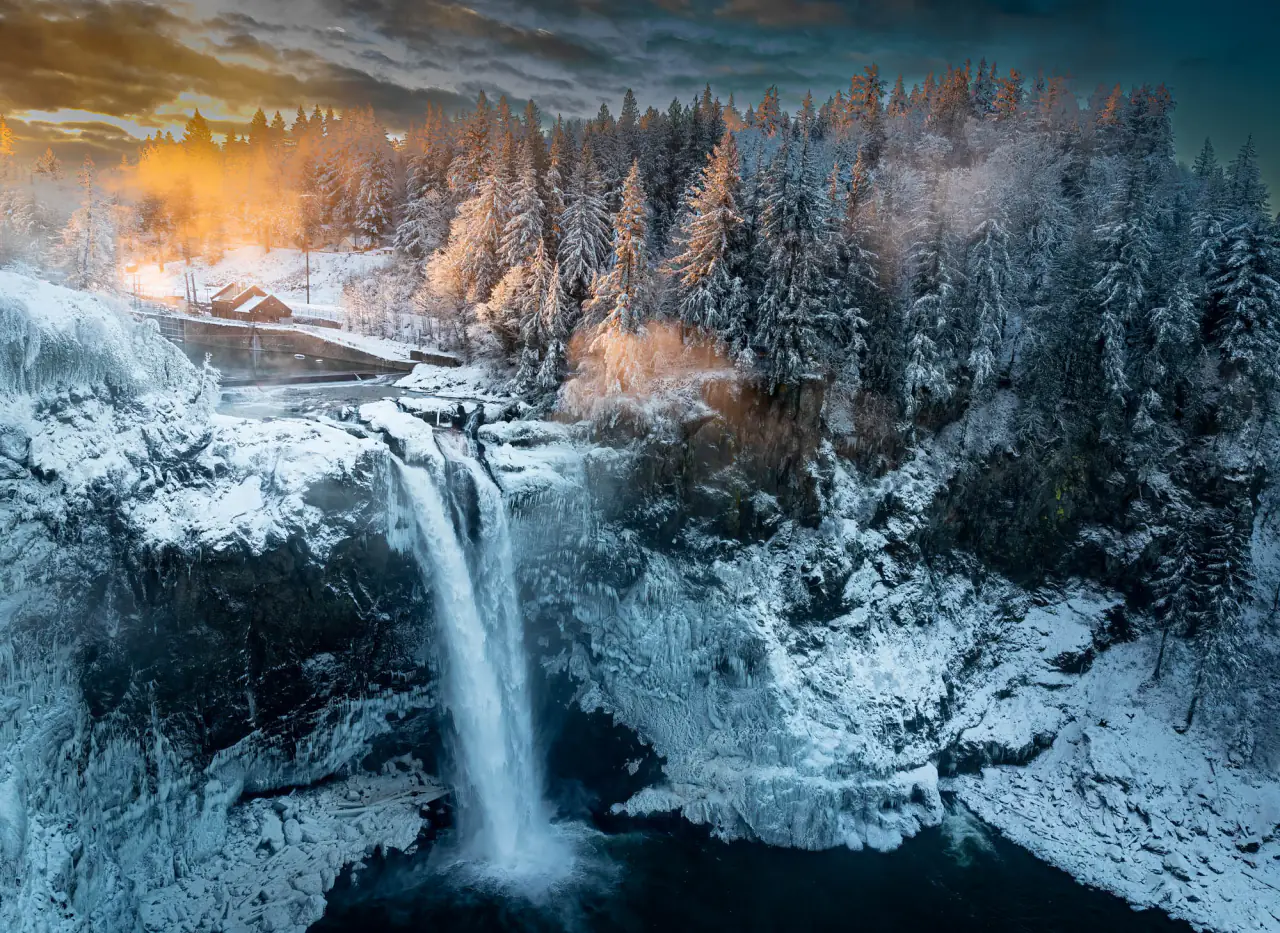 Snoqualmie Falls and its gorge covered in fresh snow under a pale orange sky