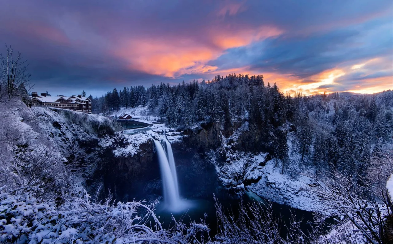Snoqualmie Falls and Salish Lodge surrounded by snow-covered trees beneath a pink and blue sky