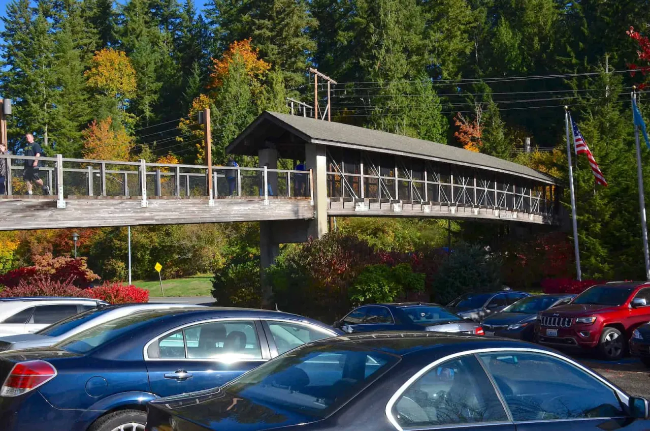 Cars parked below the covered pedestrian bridge at Snoqualmie Falls, with autumn trees behind