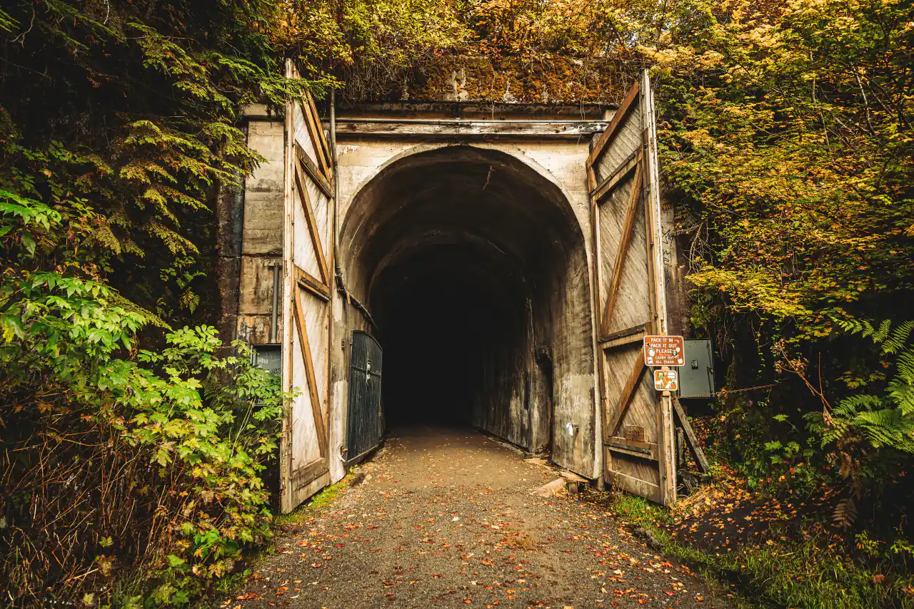 The arched concrete east portal of the Snoqualmie Tunnel with its gates open and autumn trees around it